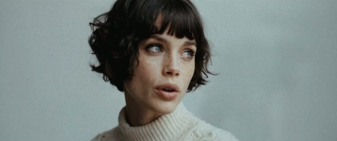 A woman with a dark fringe bob and white jumper, in black and white close-up, then in colour
